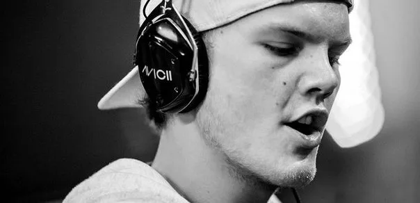 Ασπρόμαυρο κοντινό πλάνο του Avicii με ακουστικά και καπέλο.