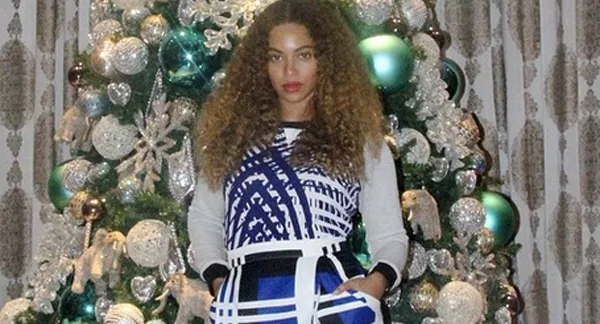 Η Beyonce ποζάρει μπροστά από ένα στολισμένο χριστουγεννιάτικο δέντρο.