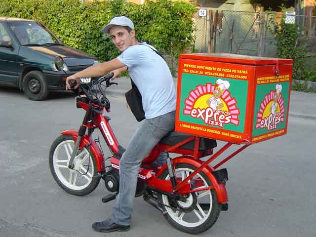 Νεαρός ντελιβεράς πάνω σε κόκκινο μηχανάκι με μεγάλο κουτί πίτσας.