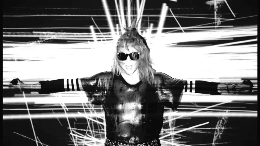Η Madonna με γυαλιά ηλίου και ανοιχτά χέρια σε ασπρόμαυρο φόντο με φωτεινές γραμμές.