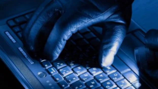 Χέρια με μαύρα γάντια πληκτρολογούν σε λάπτοπ υπό μπλε φωτισμό.