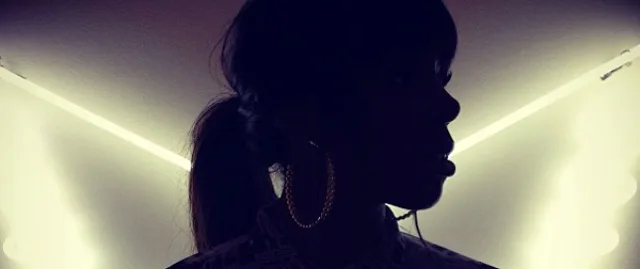 Σιλουέτα της Kelly Rowland με μεγάλους κρίκους σκουλαρίκια σε φόντο με φώτα νέον.