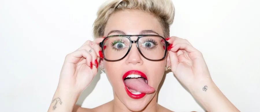 Η Miley Cyrus με γυαλιά και κόκκινο κραγιόν βγάζει τη γλώσσα της.
