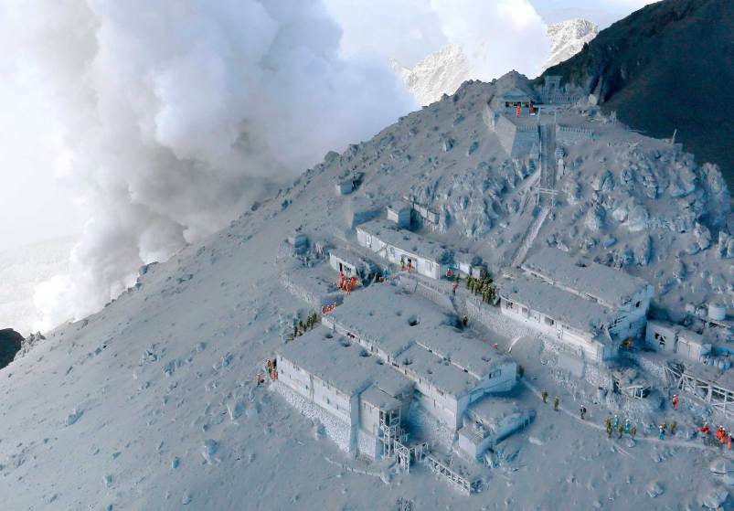 JSDF soldiers and firefighters conduct rescue operations at mountain lodges, covered with volcanic ash as volcanic smoke rises near the peak of Mt. Ontake, which straddles Nagano and Gifu prefectures