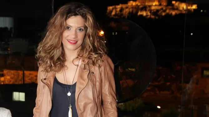 Η Σύλβια Δελικούρα με καφέ δερμάτινο τζάκετ και φόντο την Ακρόπολη.