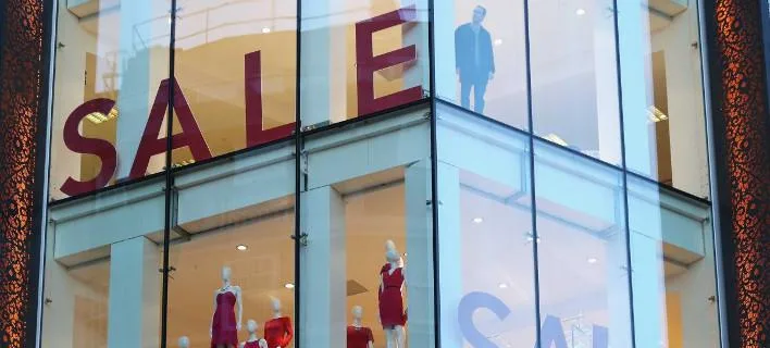 Βιτρίνα καταστήματος ρούχων με μεγάλες κόκκινες επιγραφές SALE.