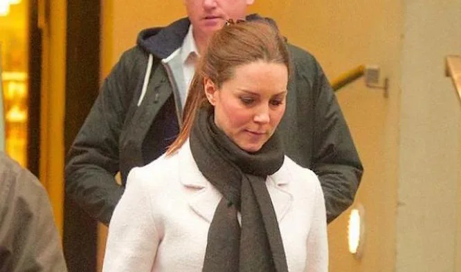 Η Kate Middleton με λευκό παλτό και γκρι κασκόλ σε εξωτερικό χώρο.