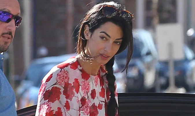 Η Amal Alamuddin με λευκό φόρεμα με κόκκινα λουλούδια και γυαλιά ηλίου στα μαλλιά.
