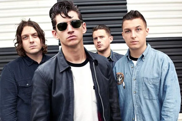 Το συγκρότημα Arctic Monkeys ποζάρει μπροστά από ριγέ φόντο.