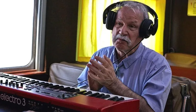 Ο Giorgio Moroder με ακουστικά μπροστά από ένα κόκκινο synthesizer.
