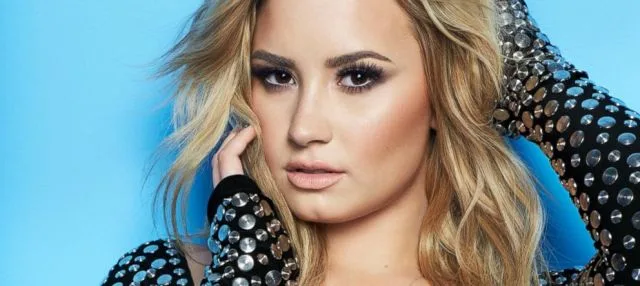 Κοντινό πορτρέτο της Demi Lovato με ξανθά μαλλιά και μαύρο ρούχο με μεταλλικά τρουκς.