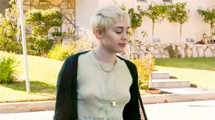 Η Miley Cyrus με κοντό ξανθό μαλλί και μαύρη ζακέτα σε εξωτερικό χώρο.