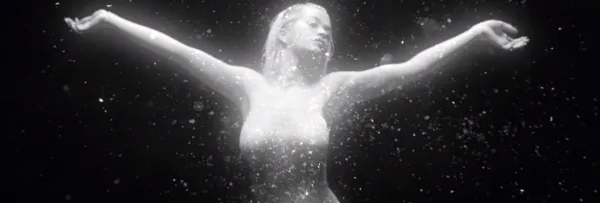 Η Rita Ora σε ασπρόμαυρο πλάνο με ανοιχτά χέρια και εφέ λάμψης.