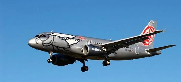 Αεροπλάνο της FlyNiki σε πτήση με γκρίζο χρώμα και σχέδιο μύγας.