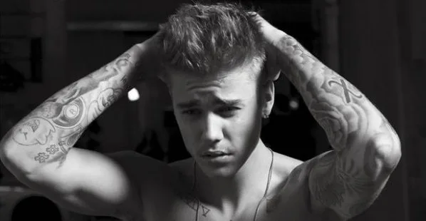Ασπρόμαυρη φωτογραφία του Justin Bieber με τα χέρια στο κεφάλι, αναδεικνύοντας τα τατουάζ στα χέρια του.