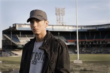 Ο Eminem με γκρι καπέλο και μαύρο τζάκετ μπροστά από ένα άδειο στάδιο.