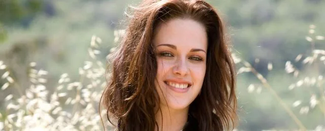Η Kristen Stewart χαμογελά σε εξωτερικό χώρο με φόντο τη φύση.