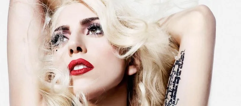 Κοντινό πορτρέτο της Lady Gaga με ξανθά μαλλιά, κόκκινο κραγιόν και τατουάζ στο μπράτσο.