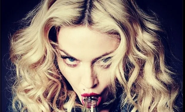 Κοντινό πλάνο της Madonna με ξανθά κυματιστά μαλλιά να κρατά ένα μπουκάλι στο στόμα.