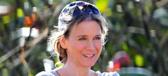 Η Renee Zellweger χαμογελάει φορώντας καπέλο σε εξωτερικό χώρο.