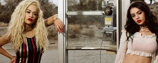 Η Rita Ora και η Charli XCX ποζάρουν δίπλα σε έναν τηλεφωνικό θάλαμο στην έρημο.