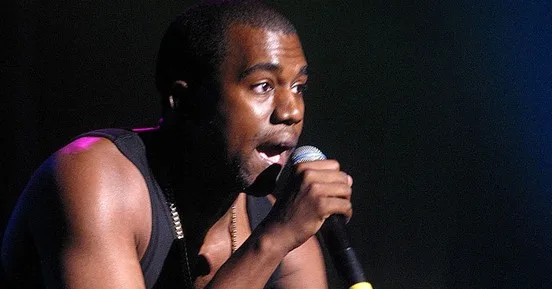 Ο Kanye West τραγουδάει σε σκηνή κρατώντας μικρόφωνο.