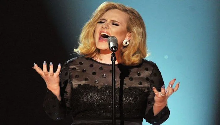 Η Adele τραγουδάει σε σκηνή με μαύρο δαντελωτό φόρεμα.