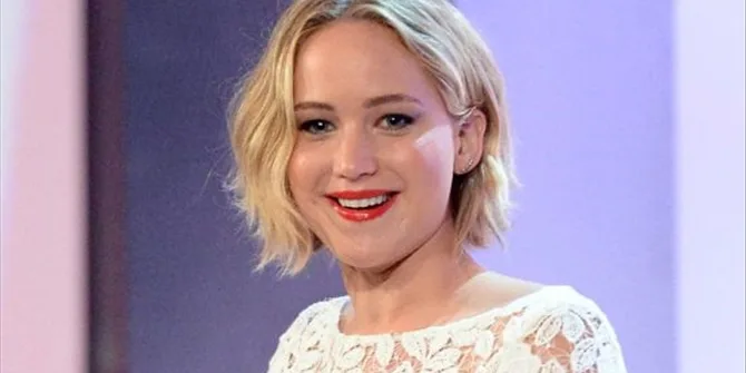 Η Jennifer Lawrence χαμογελάει φορώντας λευκό δαντελωτό φόρεμα.