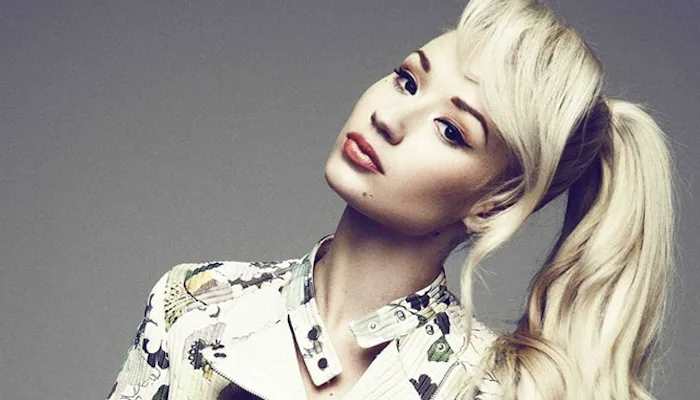 Η Iggy Azalea με ξανθά μαλλιά πιασμένα αλογοουρά και εμπριμέ τζάκετ.