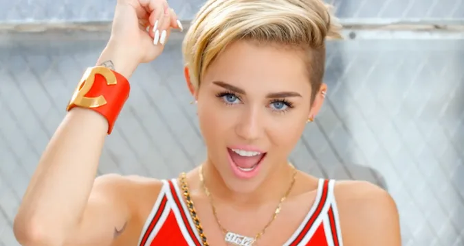 Η Miley Cyrus με κοντό ξανθό μαλλί και κόκκινο αθλητικό τοπ.