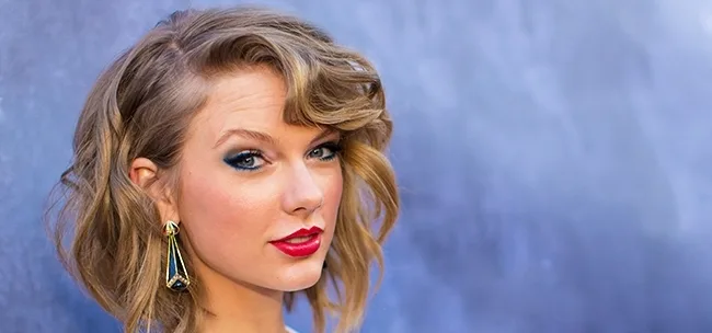 Η Taylor Swift με κοντό κυματιστό καρέ μαλλί, έντονο κόκκινο κραγιόν και μπλε σκιά ματιών.
