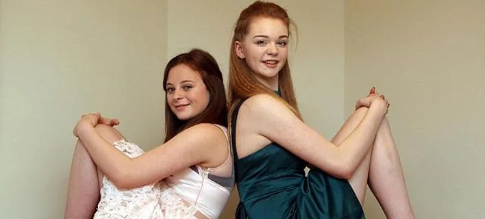 Δύο νεαρές κοπέλες κάθονται πλάτη με πλάτη στο πάτωμα.