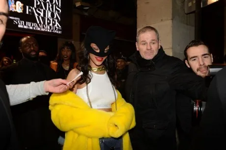 Η Rihanna με μαύρη μάσκα catwoman, λευκό crop top και κίτρινη γούνα σε εκδήλωση μόδας.