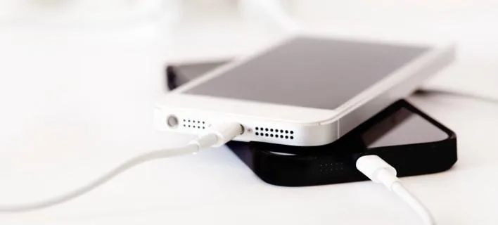 Δύο iPhone, ένα λευκό και ένα μαύρο, να φορτίζουν με καλώδια Lightning.