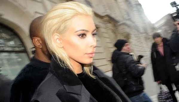 Η Kim Kardashian με πλατινέ μαλλιά και μαύρο παλτό σε εξωτερικό χώρο.
