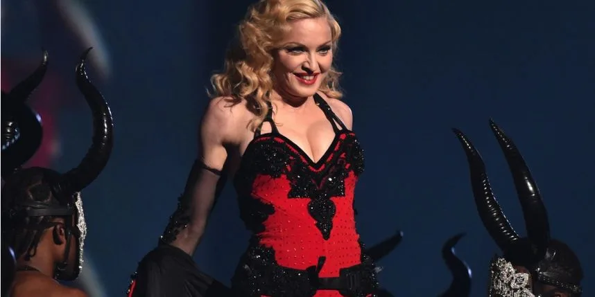 Η Madonna στη σκηνή με κόκκινο και μαύρο κορσέ ανάμεσα σε χορευτές με κέρατα.