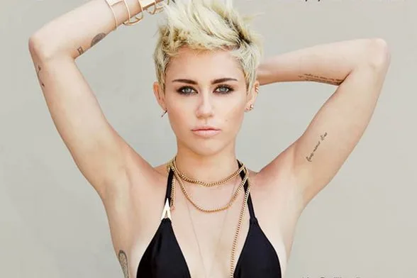 Η Miley Cyrus με κοντό ξανθό μαλλί, μαύρο μαγιό και χρυσά κοσμήματα.
