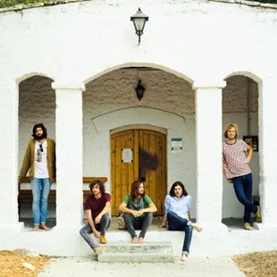 Το συγκρότημα Tame Impala μπροστά από ένα λευκό κτίριο με καμάρες.