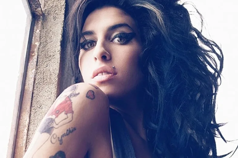 Κοντινό πορτρέτο της Amy Winehouse με το χαρακτηριστικό της χτένισμα και τατουάζ στον ώμο.