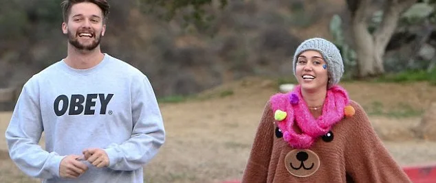 Η Miley Cyrus και ο Patrick Schwarzenegger περπατούν έξω χαμογελαστοί.