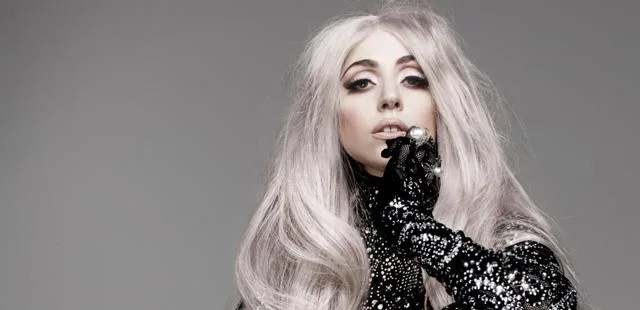 Η Lady Gaga με μακριά πλατινέ μαλλιά και μαύρο κεντητό ρούχο.