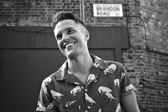 Ο Brandon Flowers χαμογελά σε ασπρόμαυρο φόντο.
