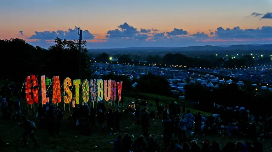 Η εμβληματική πινακίδα Glastonbury σε λόφο με θέα το φεστιβάλ κατά το σούρουπο.