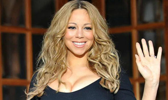 Η Mariah Carey χαμογελά και χαιρετά με το χέρι της.