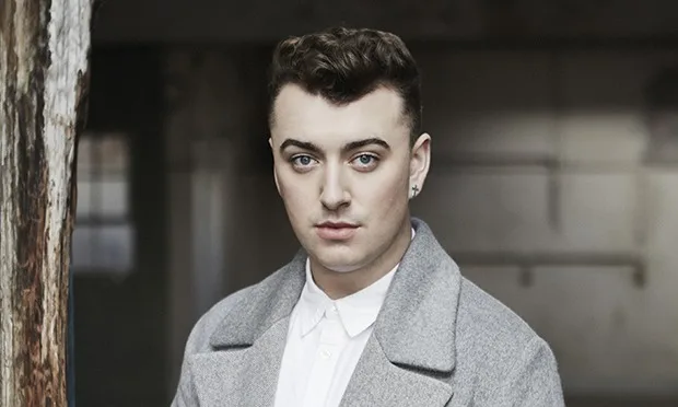 Ο Sam Smith με γκρι παλτό και λευκό πουκάμισο.