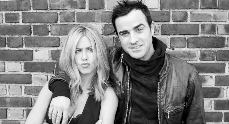 Η Jennifer Aniston και ο Justin Theroux ποζάρουν μπροστά από έναν τοίχο με τούβλα.