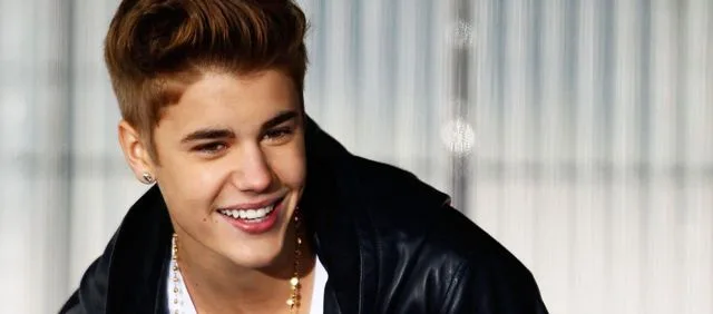 Ο Justin Bieber χαμογελάει φορώντας μαύρο δερμάτινο μπουφάν και χρυσή αλυσίδα.