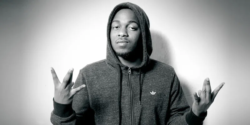 Ο Kendrick Lamar με γκρι φούτερ με κουκούλα κάνει χειρονομίες με τα χέρια του.