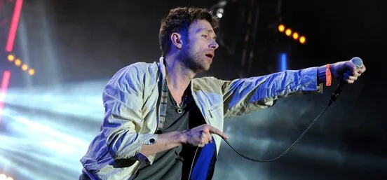Ο Damon Albarn των Blur τραγουδάει στη σκηνή κρατώντας το μικρόφωνο.