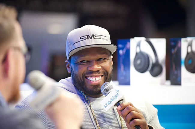 Ο 50 Cent χαμογελάει κρατώντας μικρόφωνο σε συνέντευξη.